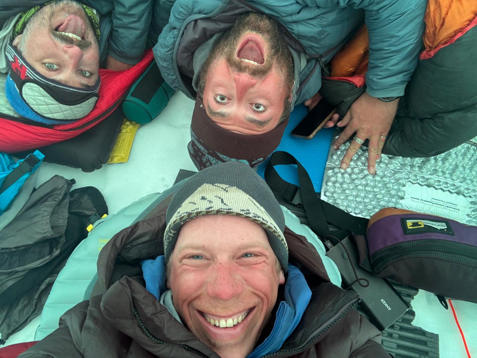 3 rangers in full winter gear shown from above laying on the ground with joyful expressions