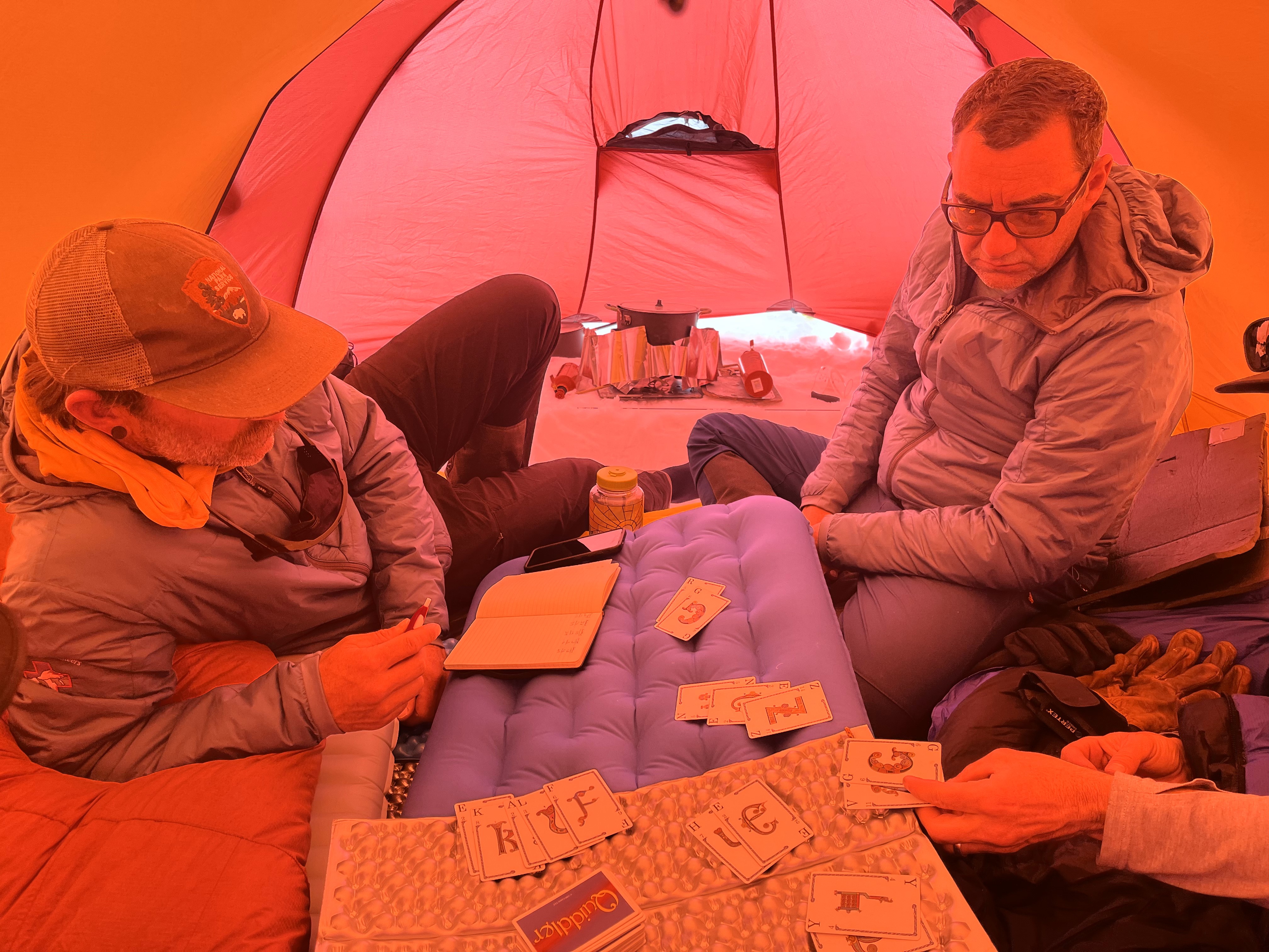 2 rangers wearing mirrored ski glasses and down coats pose in front of red tent and a snow covered mountain