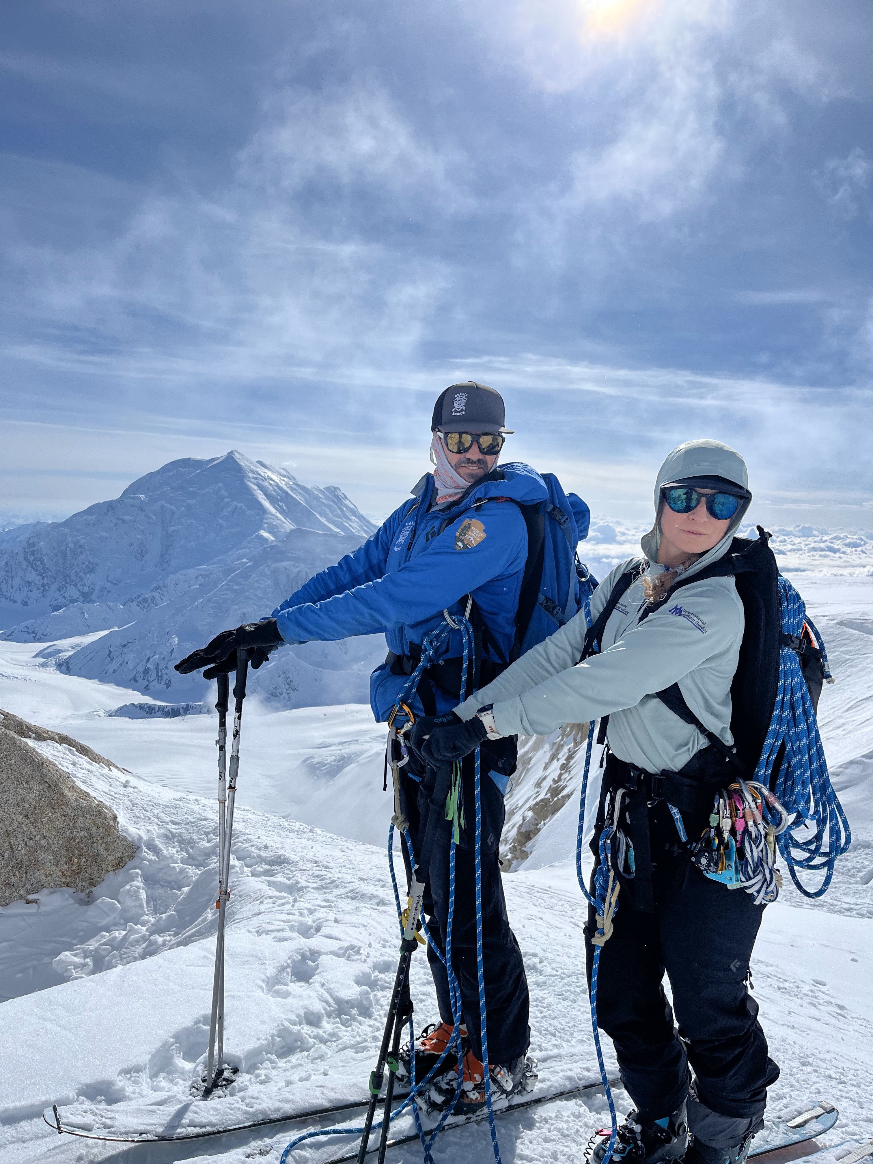 2 rangers stand together on skis with winter gear in front of a snow covered mountain
