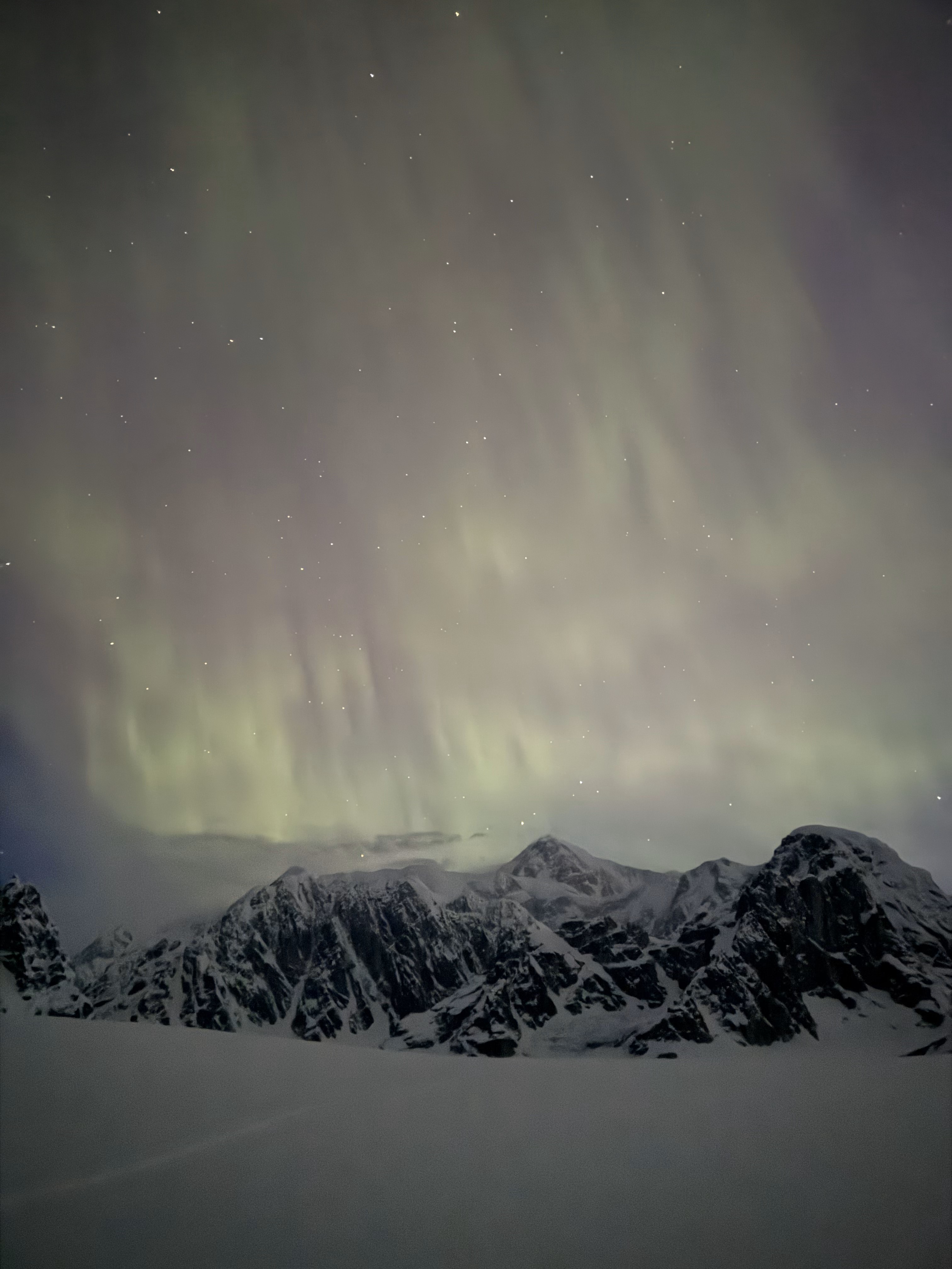Night sky with pale green northern lights above mountain peaks