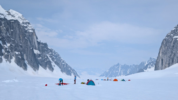 Mountaineers and tents on a snowy field between to mountain peaks