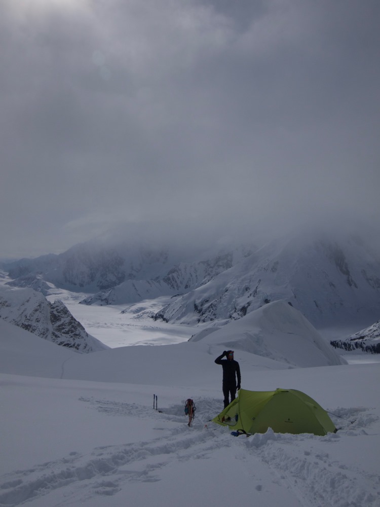 Ranger standing outside a tent with peaks and glaciers in the background