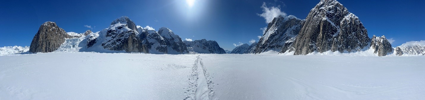 Wide shot of a glacier up against a blue sky and bright white sunshine. 