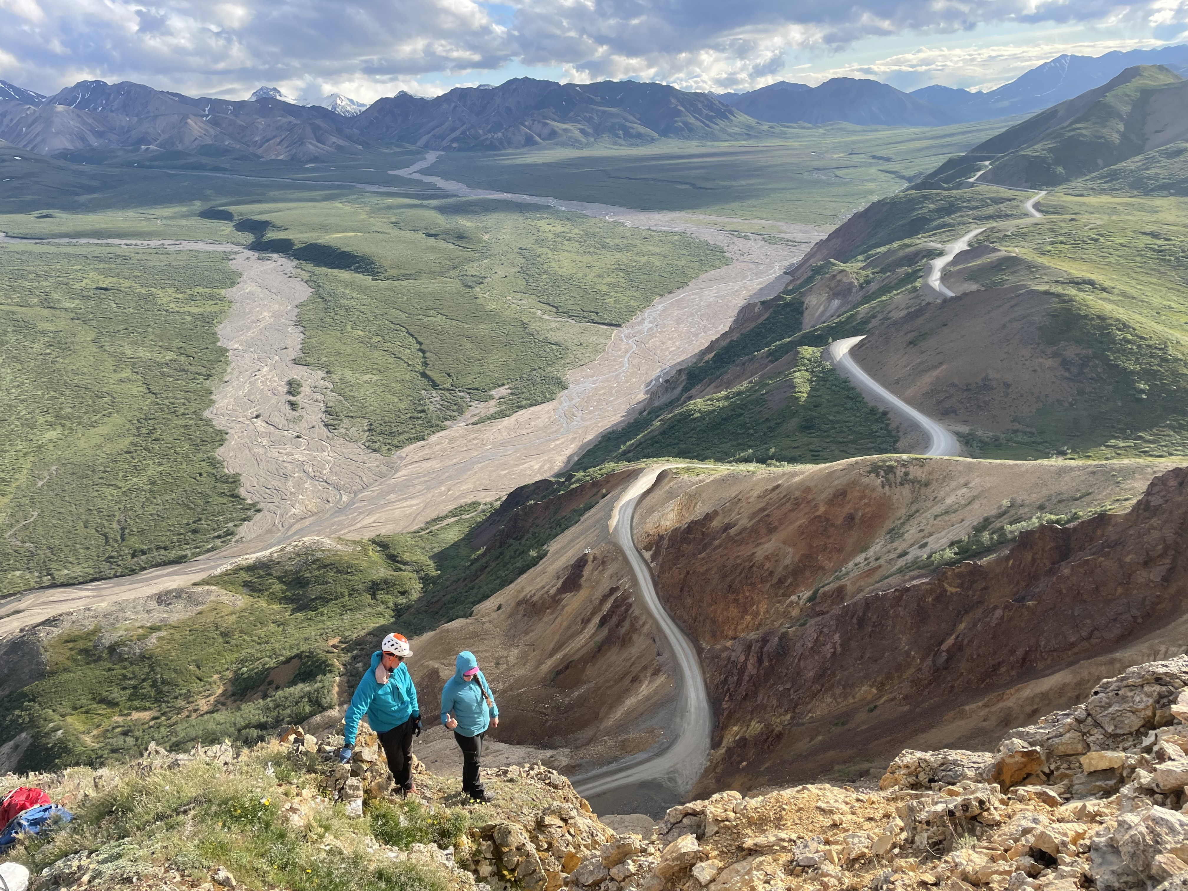Two climbers have a conversation on a rocky ridge overlooking a vast braided river valley