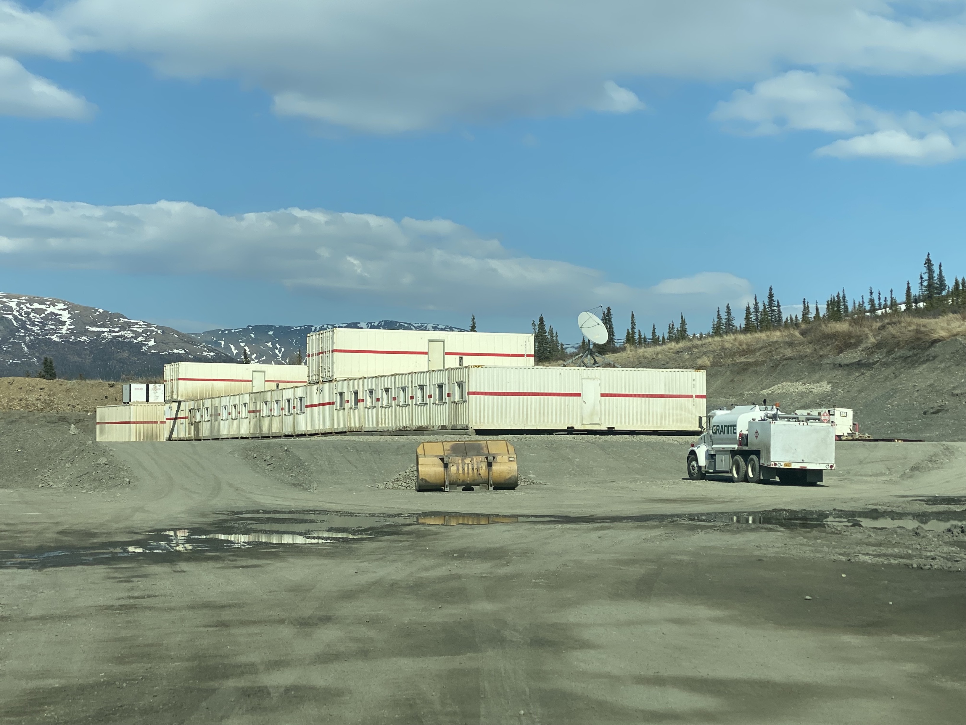Many mobile trailer buildings are connected side by side into a large unit. The unit is located in a large gravel pit with a few construction vehicles parked nearby.
