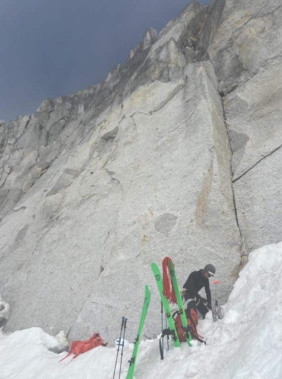 A ranger stands next to a rock face with two pairs of green skis