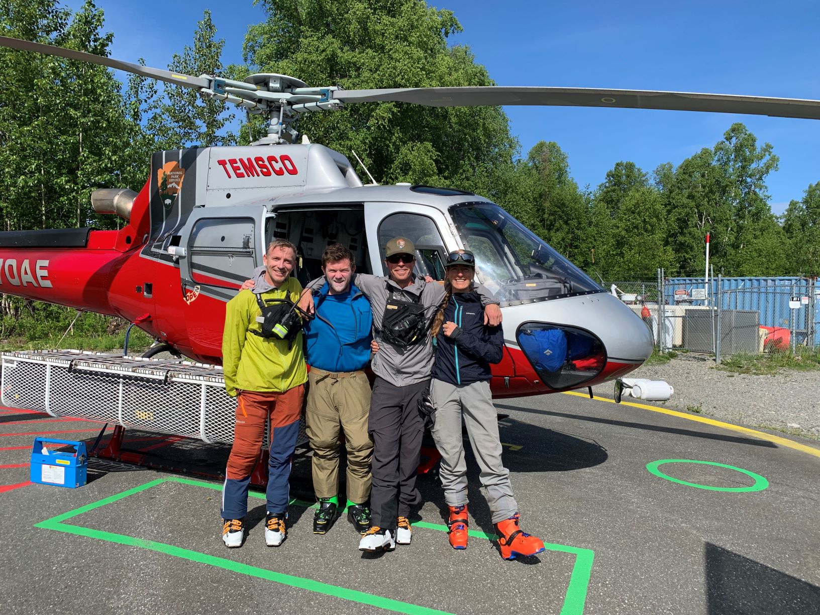 Four colorfully clad climbers stand outside a helicopter