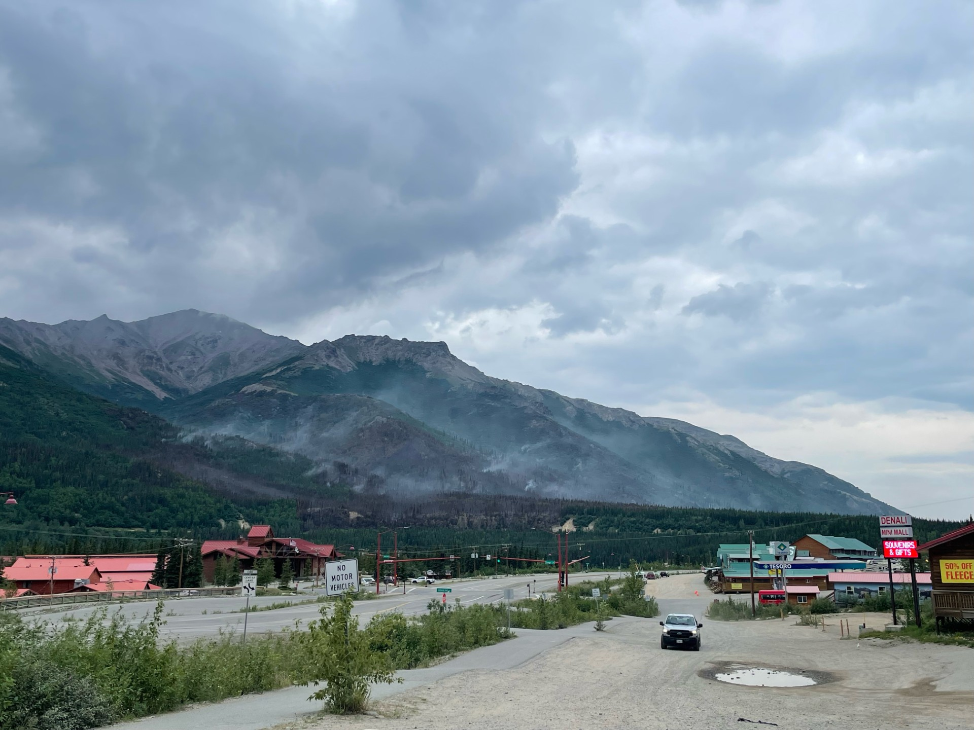 Smoke rises from mountainous terrain with buldings and roads in the foreground.