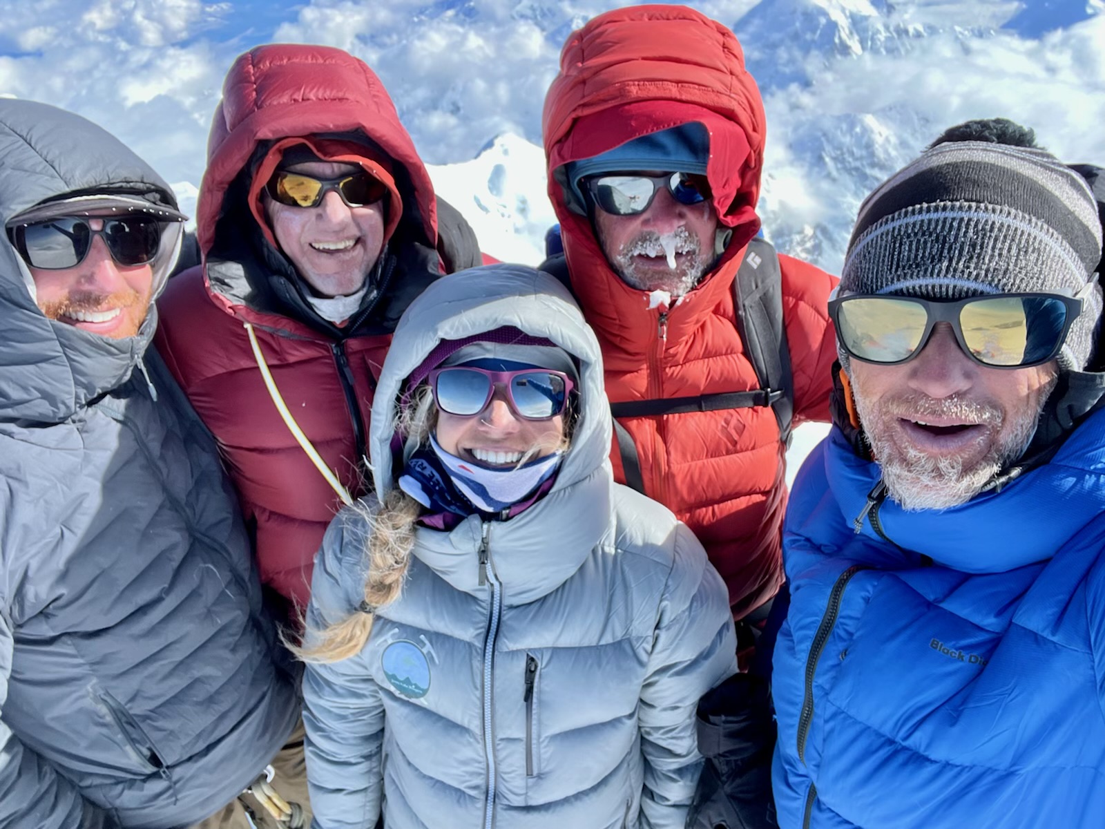 Five well-bundled and frosty climbers smile take a selfie on the summit