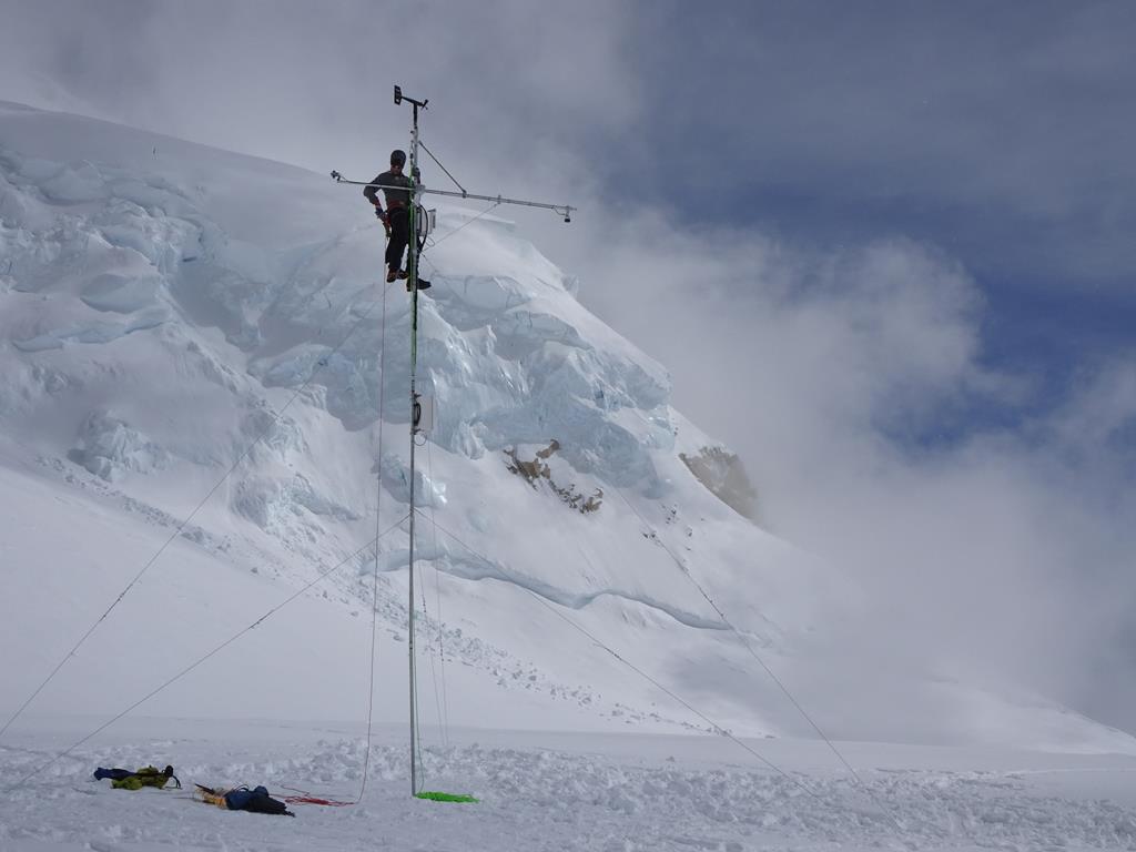 A park ranger climbs a tall metal pole to install weather equipment 