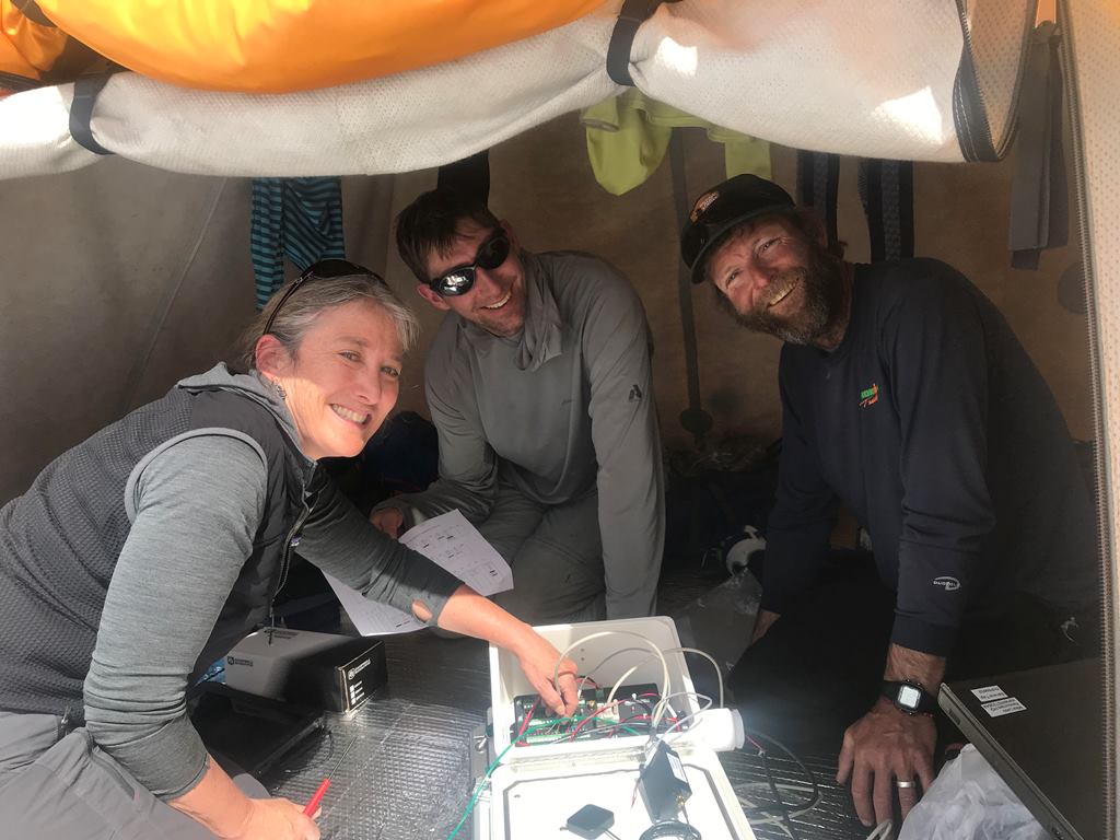 Three scientists troubleshoot the weather station equipment in a tent at Basecamp