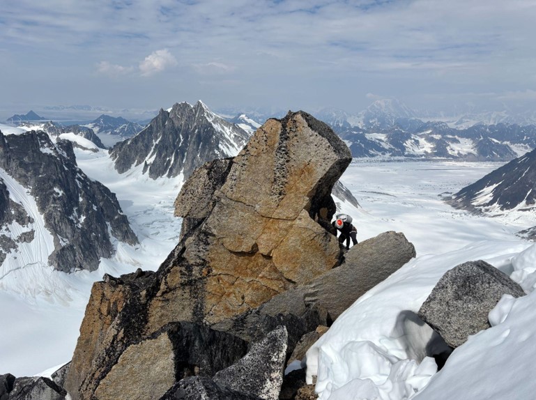 Ranger climbs a rocky outcrop with the mountain range in the distance
