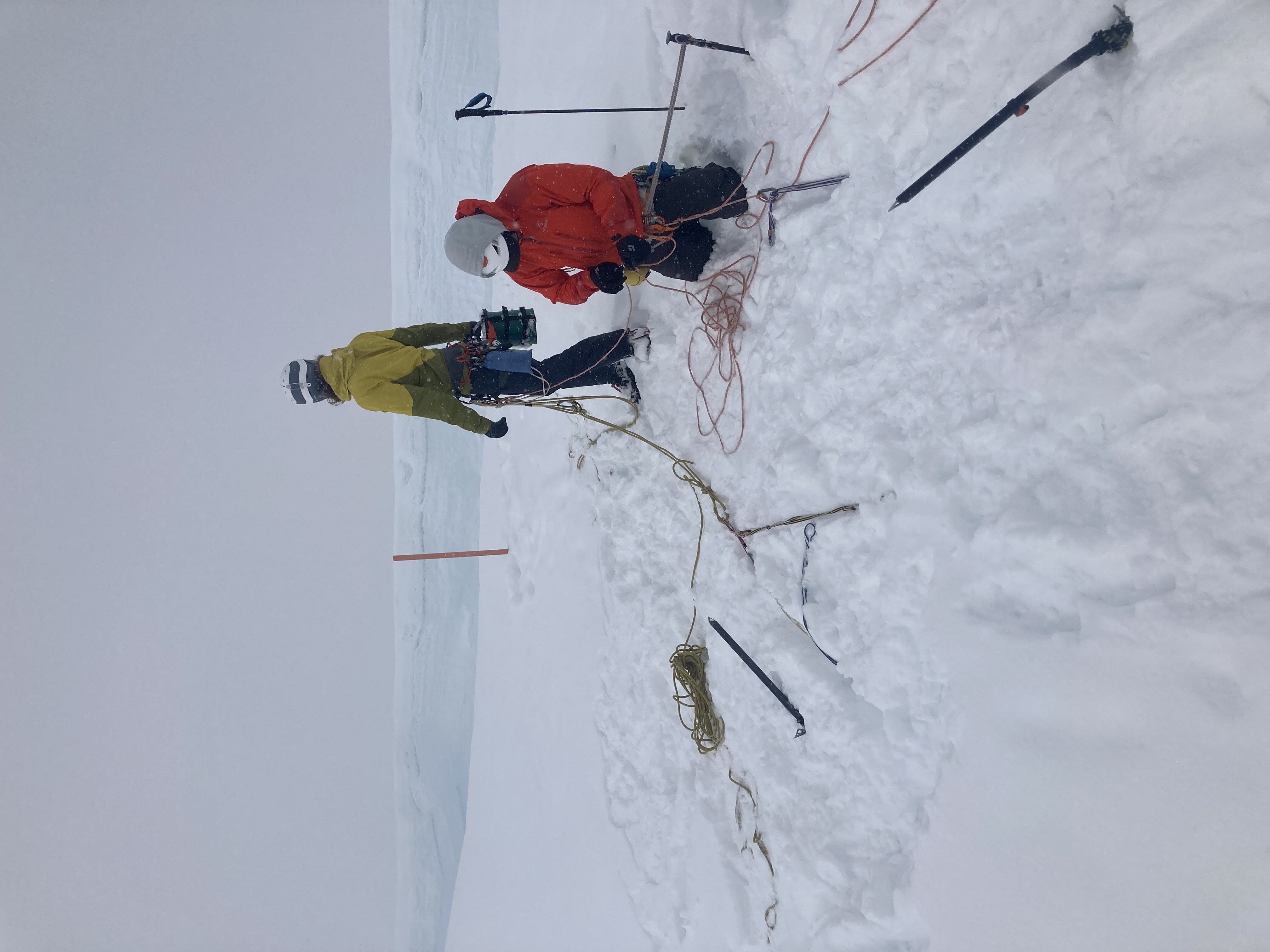 Two climbers rig up a rope system near the edge of a crevasse 