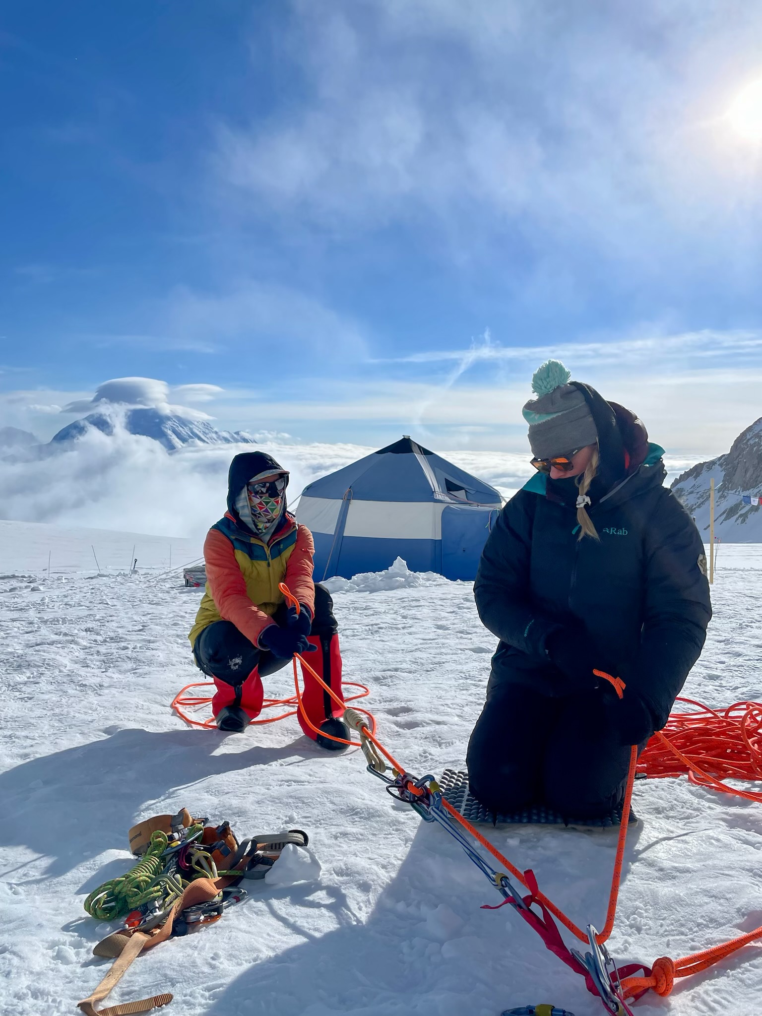 Two kneeling women set up a rope rigging system on a glacier
