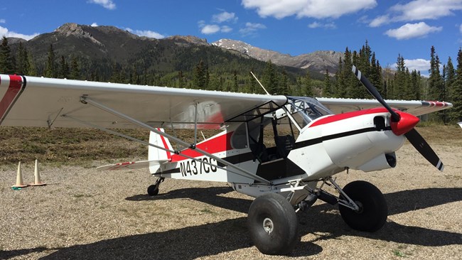 A small red and white plane with a propeller sitting on gravel