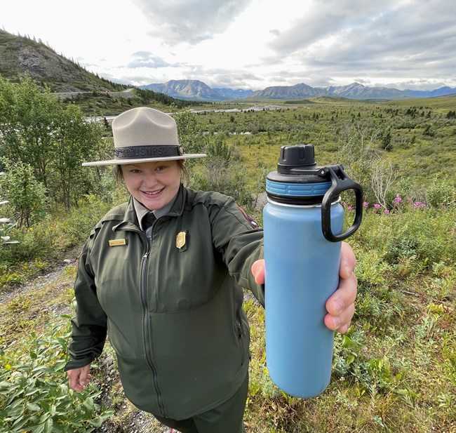 A ranger in a flat hat holds out a blue, reusable water bottle.