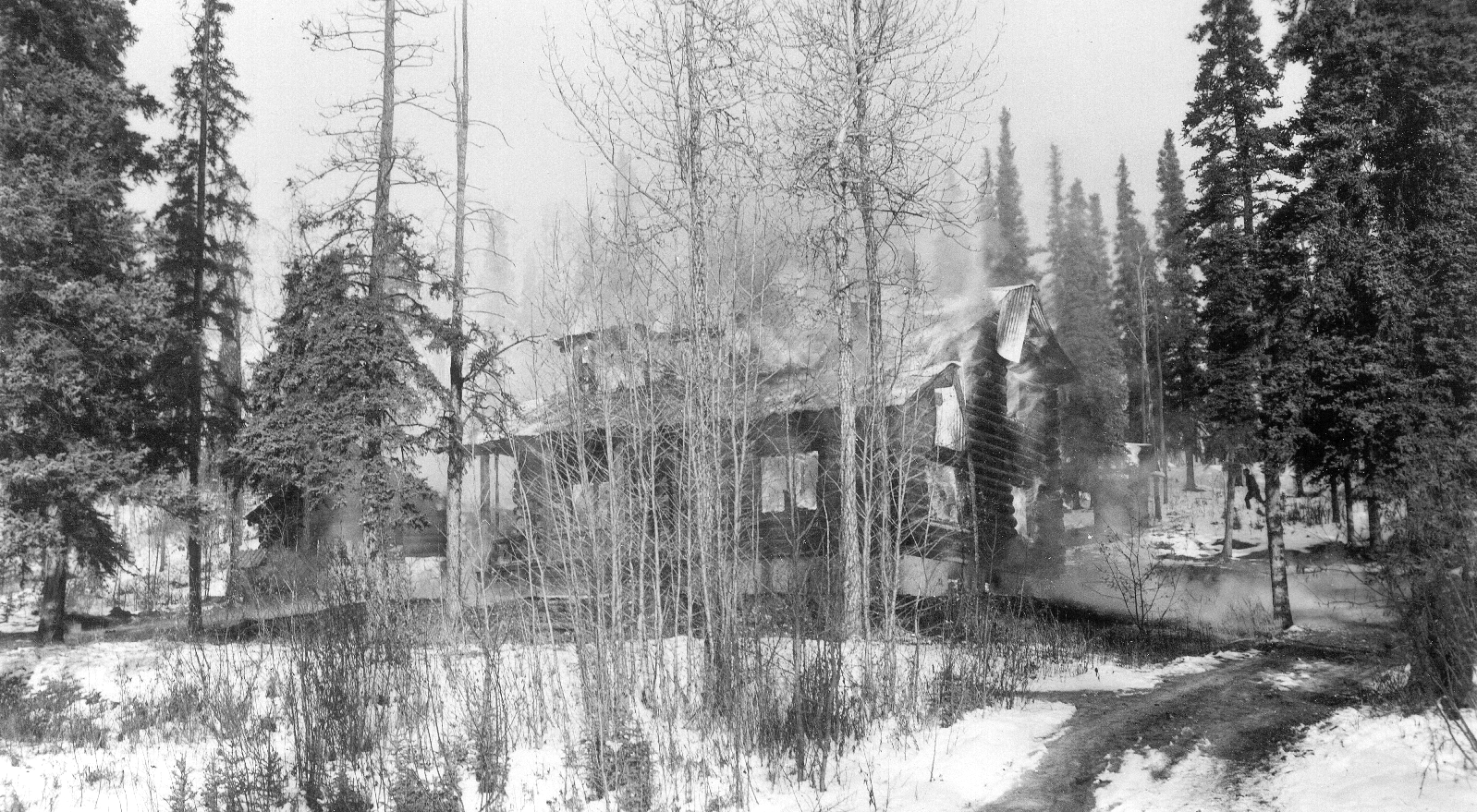 black and white image of a partially burnt building in a snowy forest