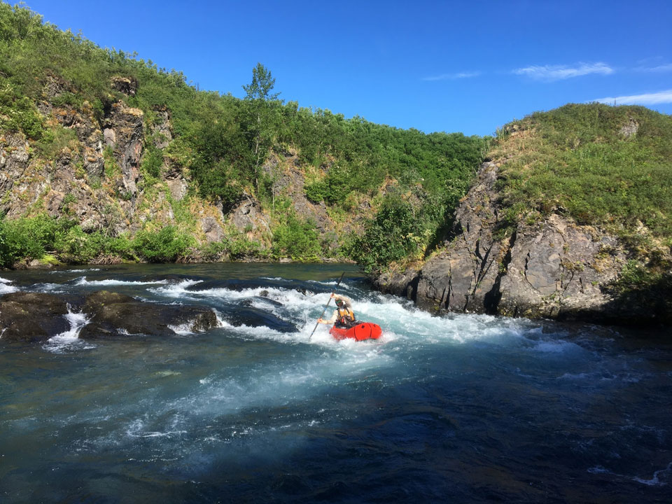 man floating in a raft through a small rapid on a creek