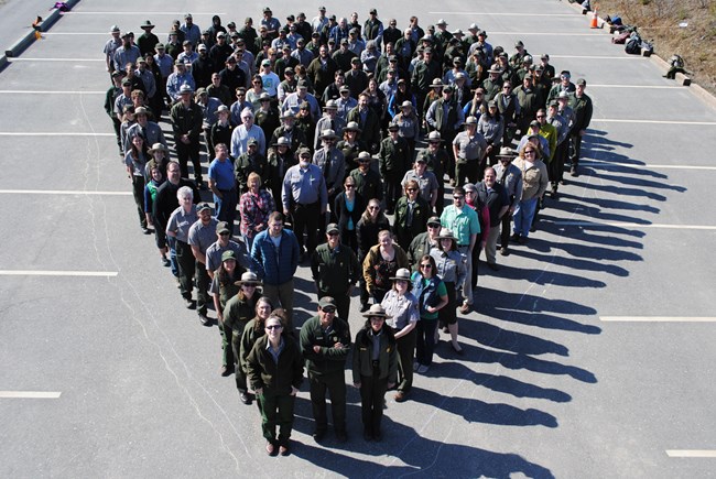 many people in green uniforms standing in a group, forming the shape of an arrowhead