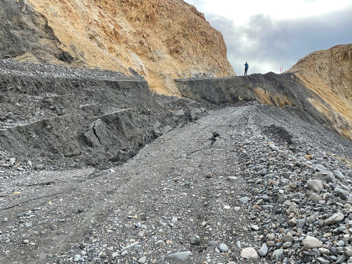 a gravel road on a mountainside, with an enormous fracture causing a big drop in the road bed