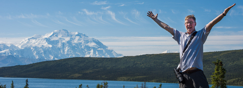 a man has his arms up with excitement, Denali is in the background