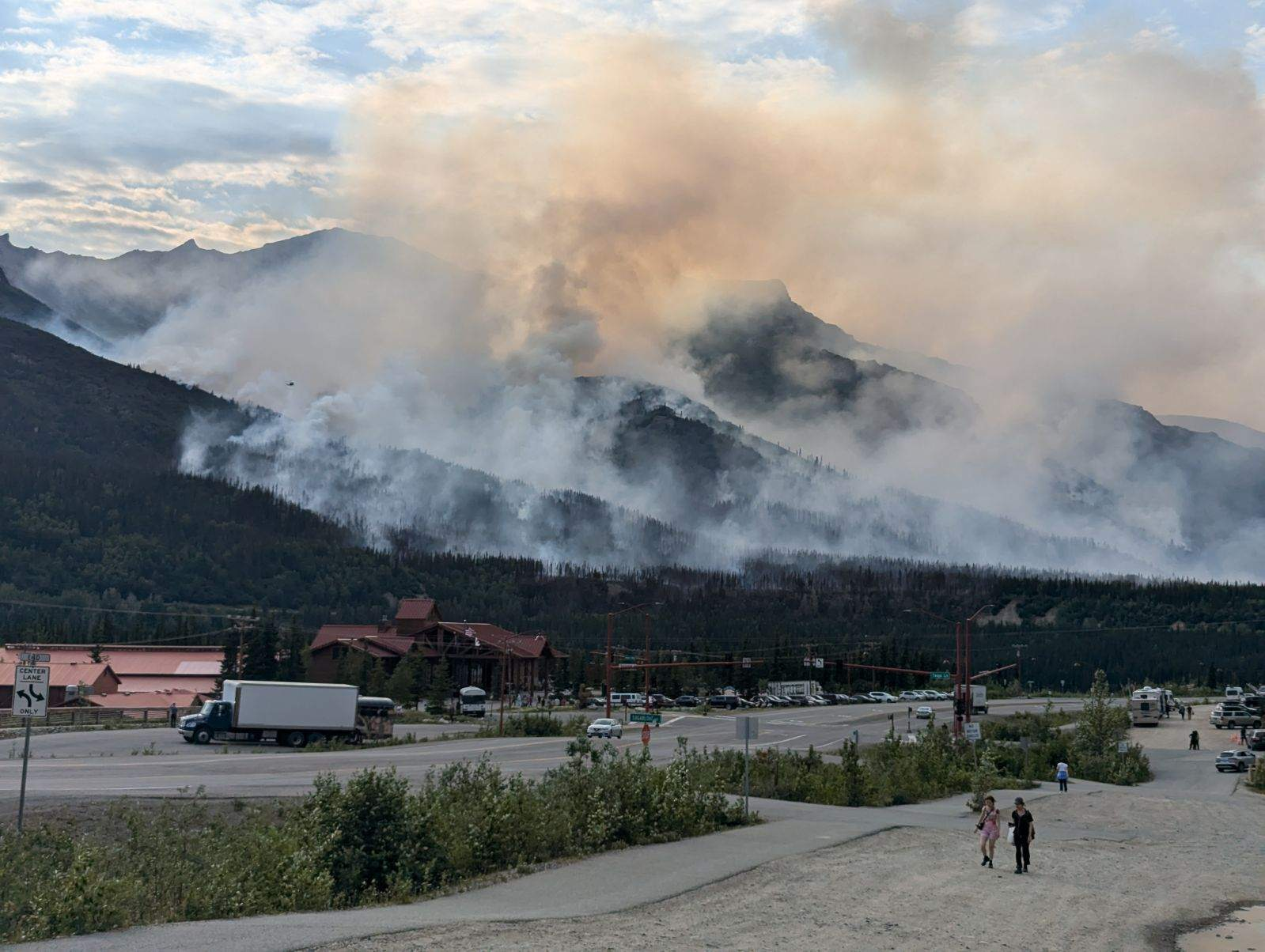 Heavy smoke rises from forested mountains near a commecial area.