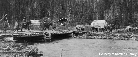 Riders on horseback crossing a creek via a wooden bridge