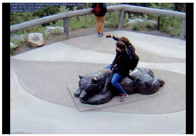 two people sitting on a bear sculpture taking a selfie