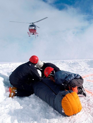 Climbers with a backboarded patient watching helicopter land
