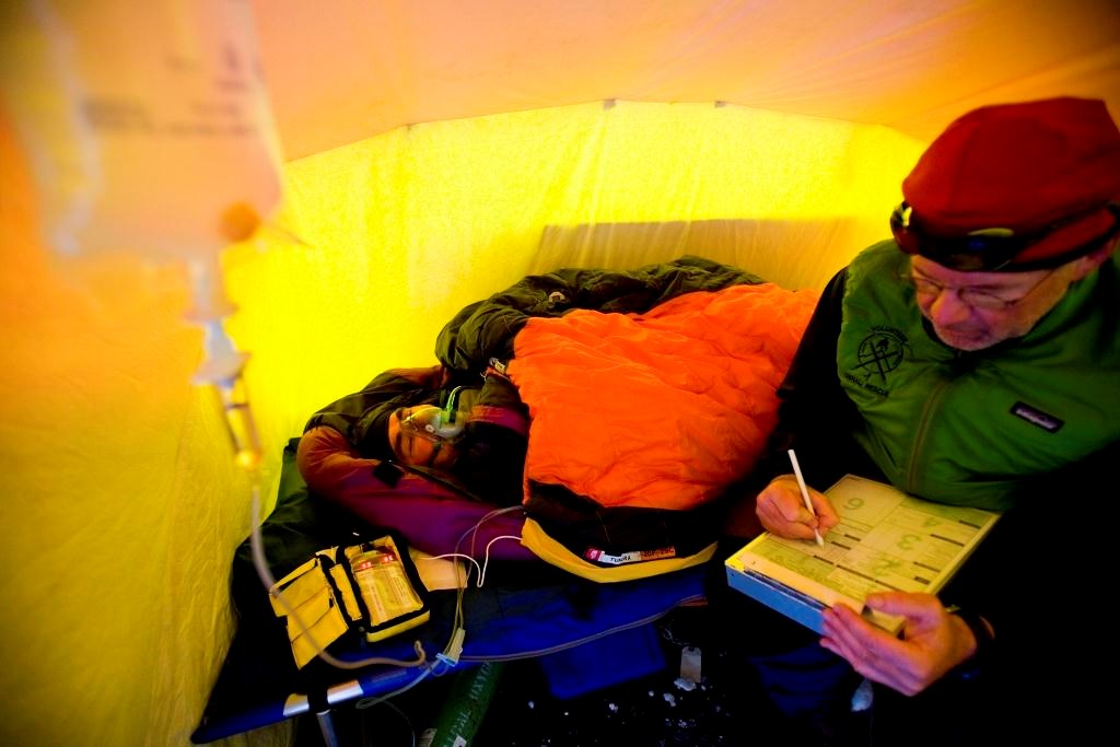 Physician seated in a tent next to a patient wearing anoxygen mask