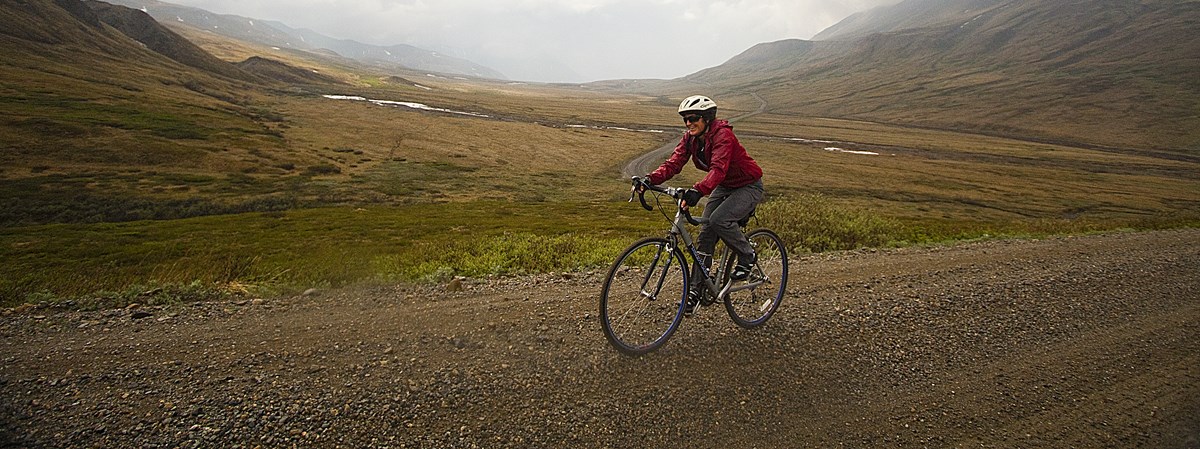 A person rides a bike down a gravel road past a vast valley.