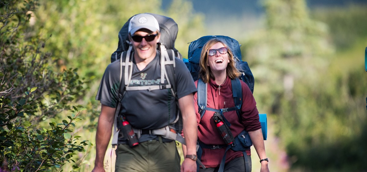 two backpacker smile as they walk down a path