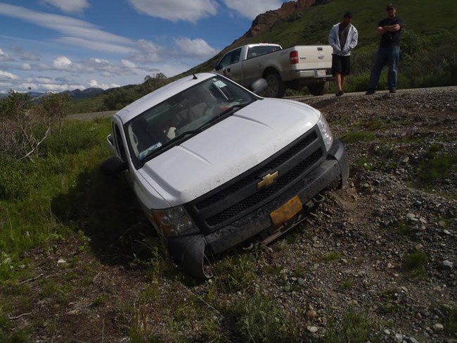 a white pickup truck in a ditch on the side of a dirt road