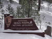 Snow accumulates on the entrance sign, which reads "Entering Devils Postpile National Monument."