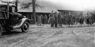 Black and white photo of a group of men standing outside a log structure