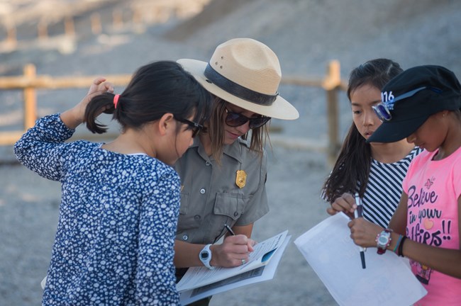 A park ranger writes on a Junior Ranger book with three young people.