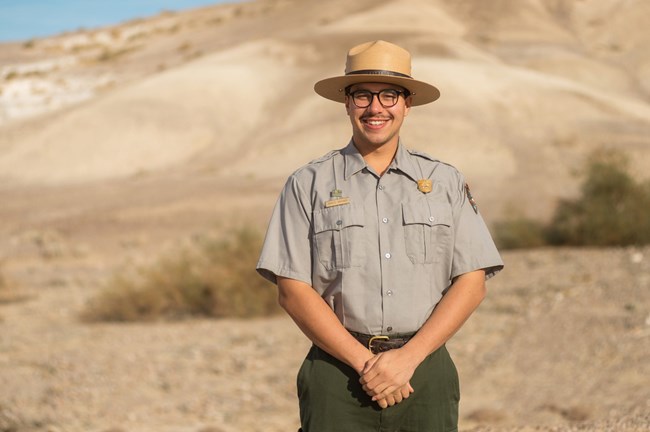 A ranger with a flat hat stands in front of a tan hill facing forward.