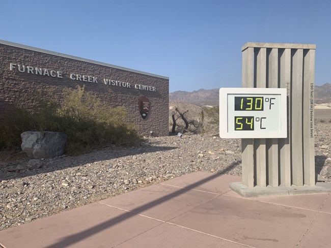 A thermometer reads 130 degrees Fahrenheit and 54 degrees Celsius in front of a building that reads "Furnace Creek Visitor Center"