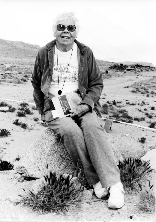 A black and what photo of a woman sitting on a rock in desert landscape