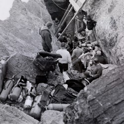 Black and white image of divers and gear around a small pool of water surrounded by natural rock walls.