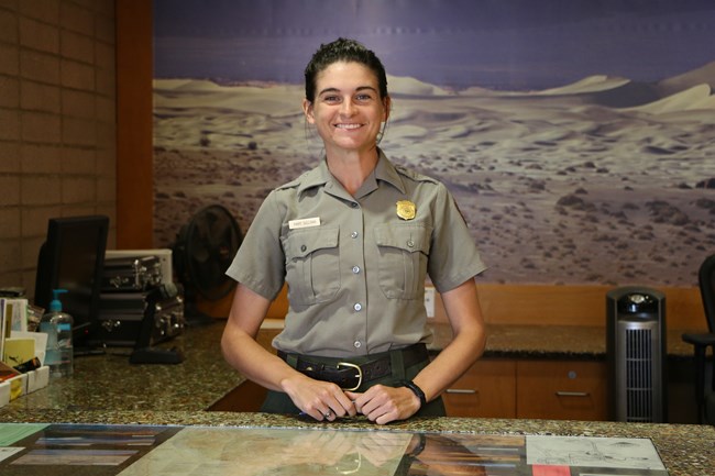 A smiling ranger stands behind a long desk.