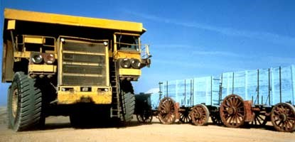 A large yellow mining vehicle dwarfs a historic, blue-painted wooden twenty mule team wagon.