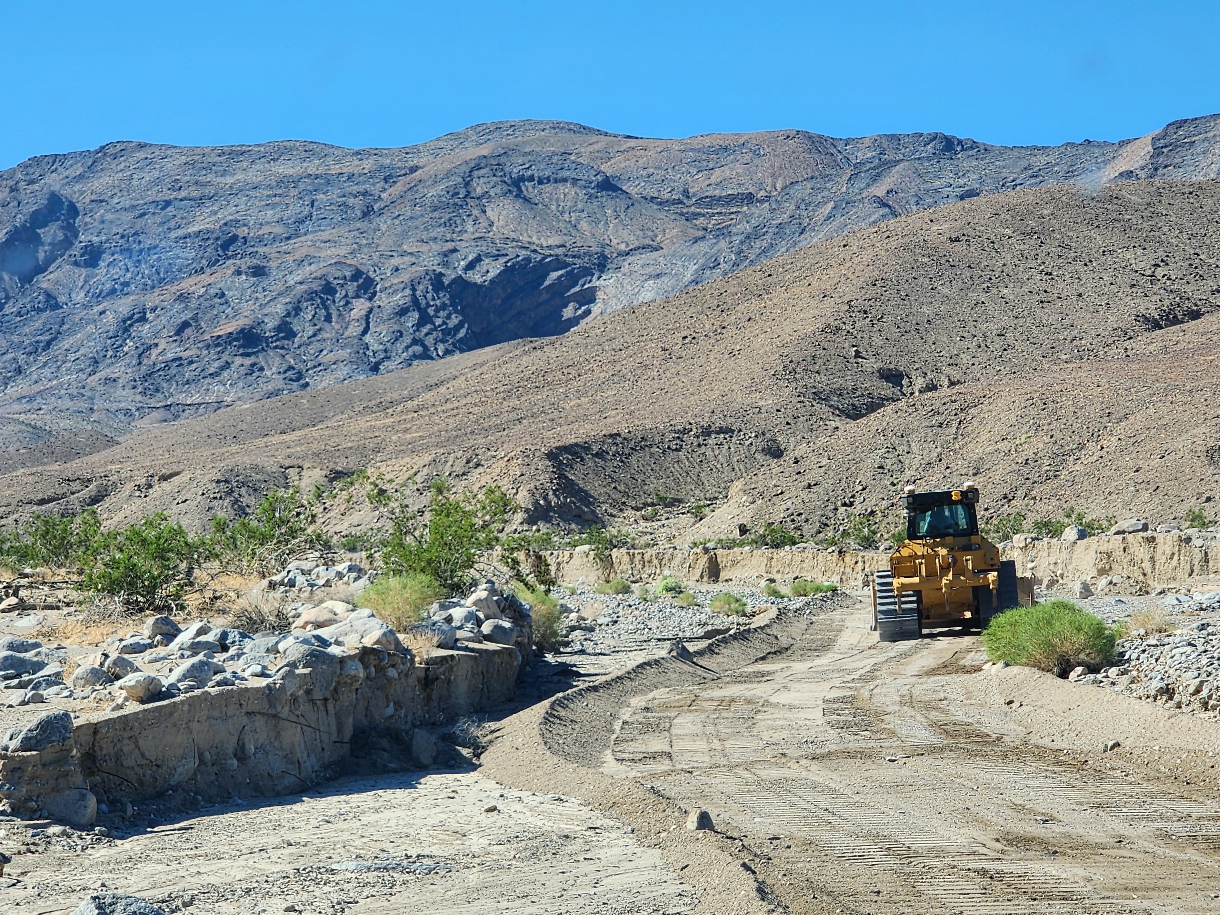 A yellow bulldozer clears fresh road surface.