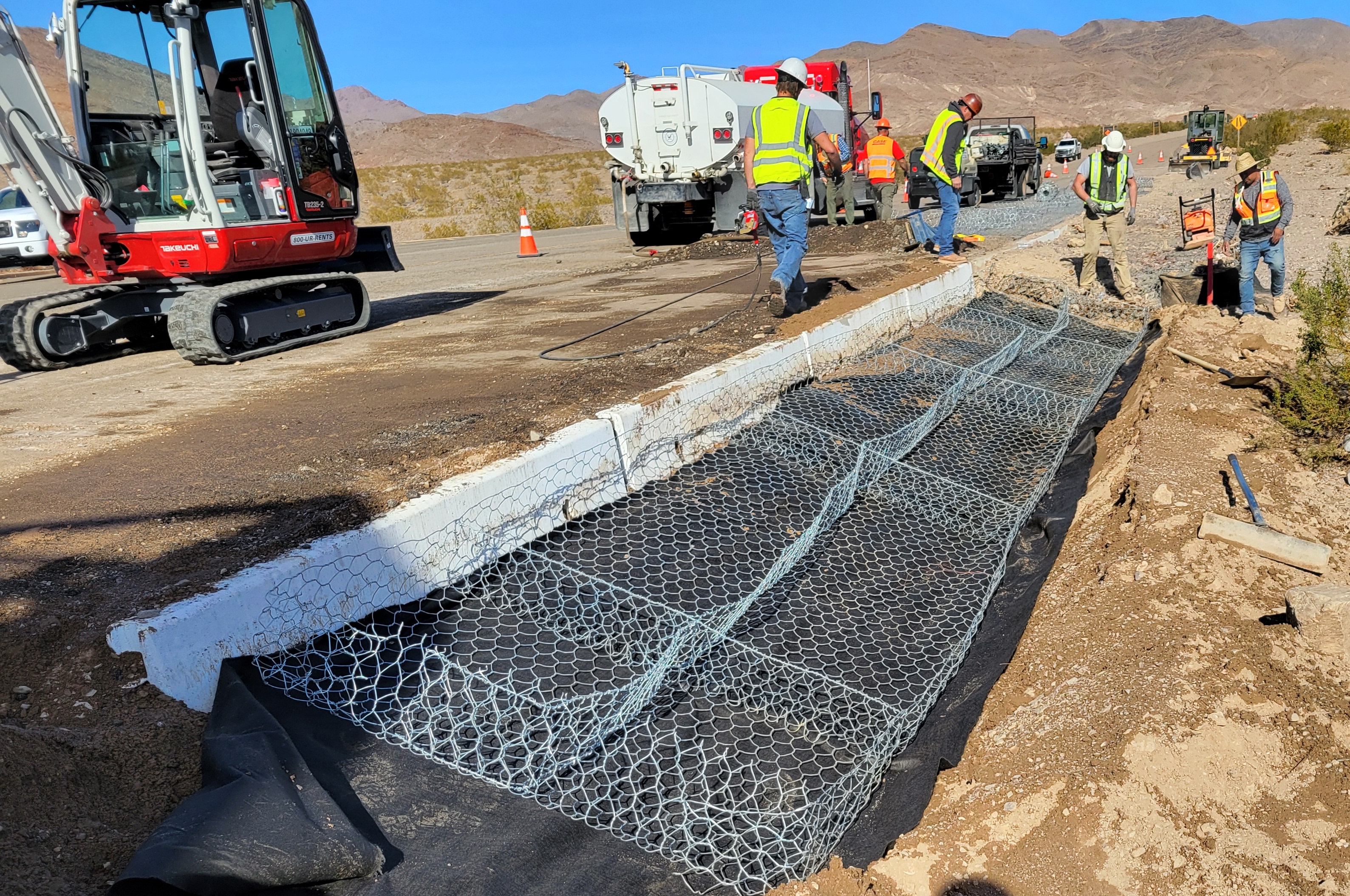 People and equipment cluster around empty wire baskets on black fabric.