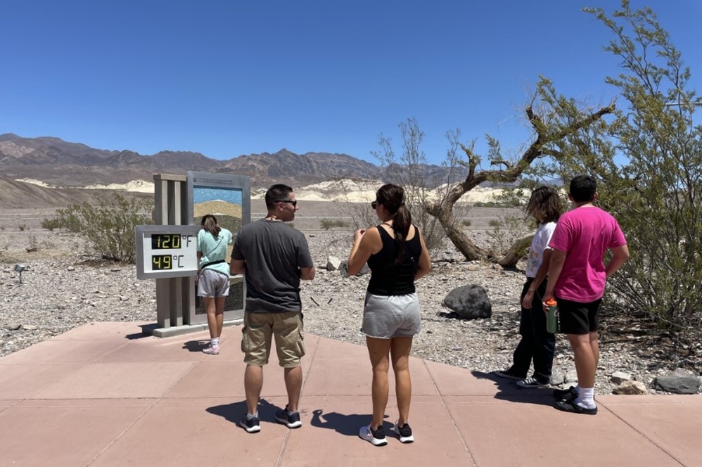 Five visitors stand in front of a digital thermometer reading 120 Fahrenheit