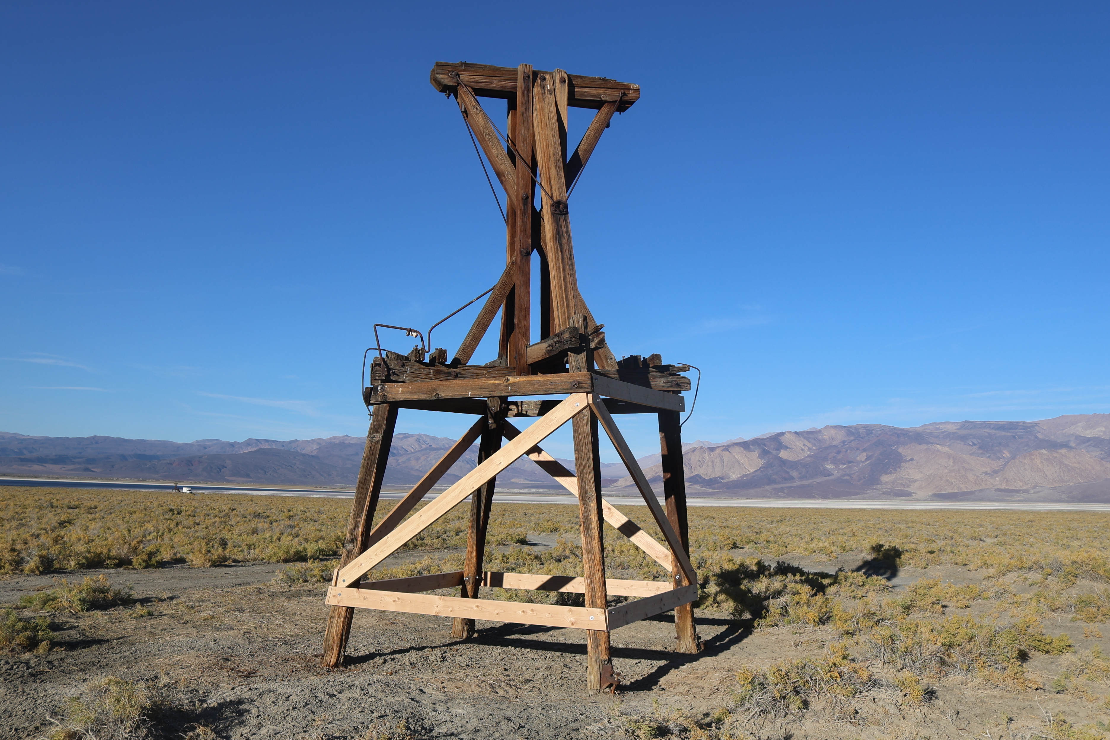 Light-colored new wood braces the four legs of a wooden tower. The original weathered wood is dark in color.