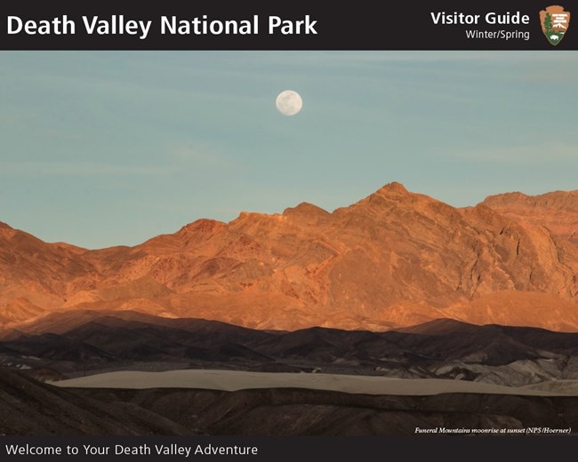 A moon rises above golden-colored desert mountains.