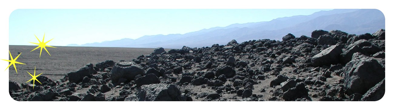 Black rocks scattered over a hill with mountains in the background.