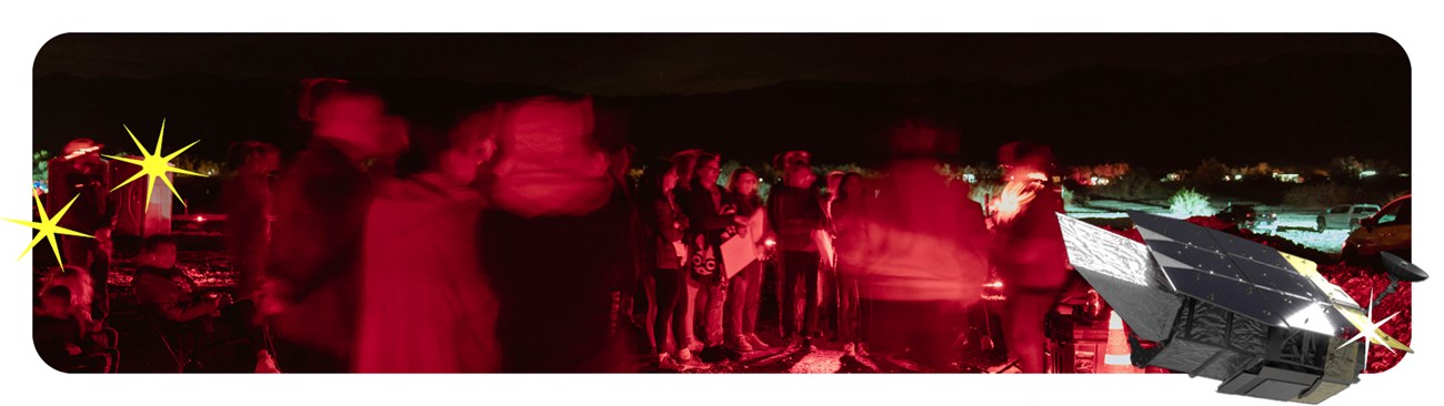 A crowd standing around a ranger in the dark, everyone is illuminated by red light.