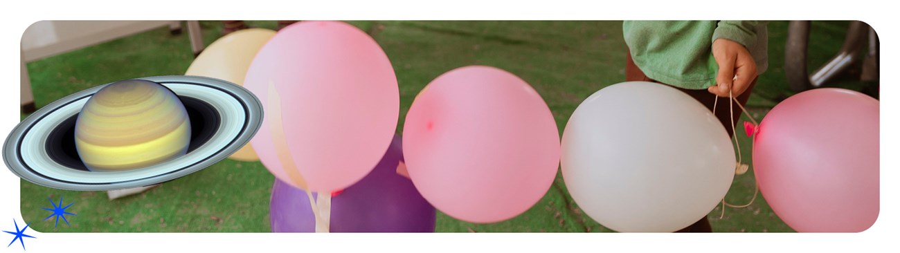 A close up of a child's hand holding colorful balloons and a cutout of Jupiter on the side of the photo.